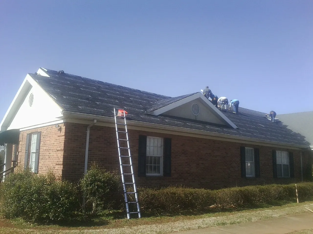 Crew tearing shingles off a brick ranch roof with a ladder set — Metal Roof Repair work by our crew in Paramount