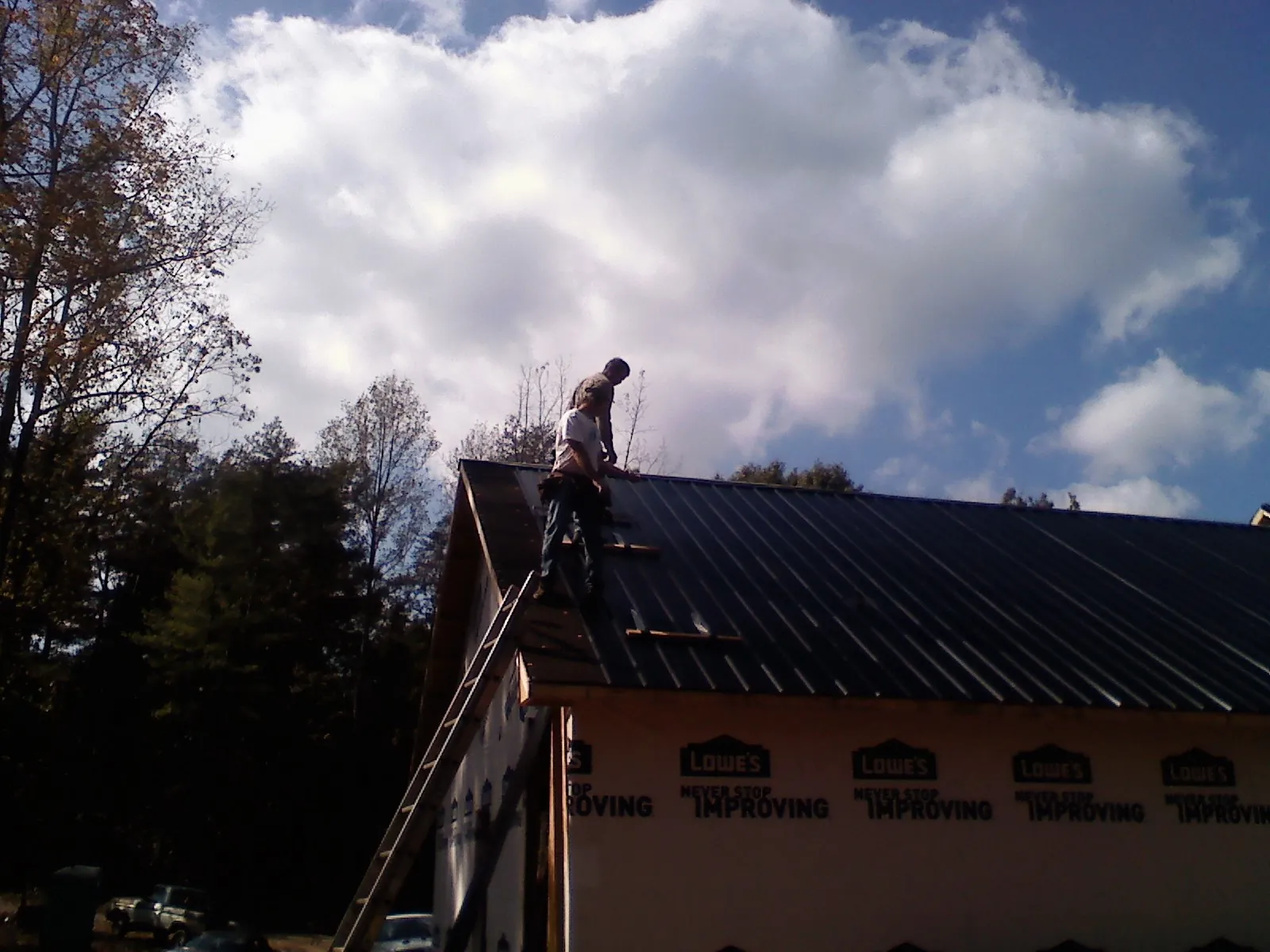 Roofer fastening dark metal panels high against a cloudy sky, from a Roof Inspection job in Paramount